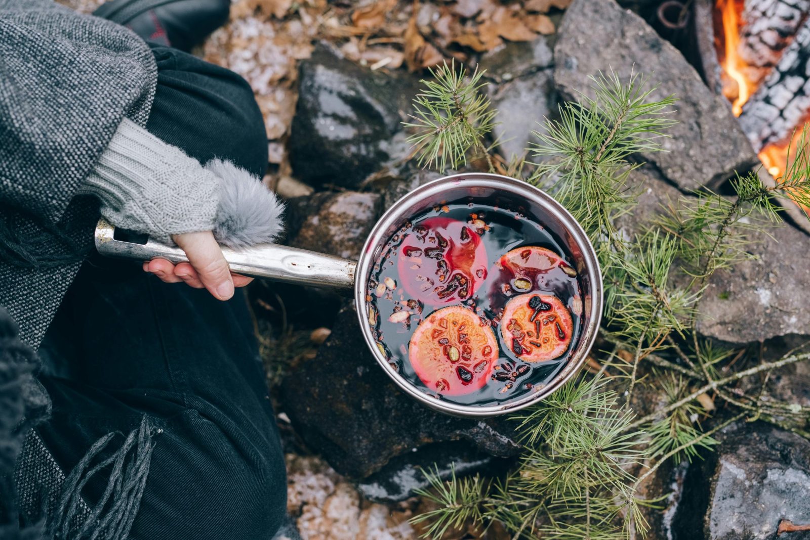 Top view of mulled wine with oranges in a pot by a campfire during winter.