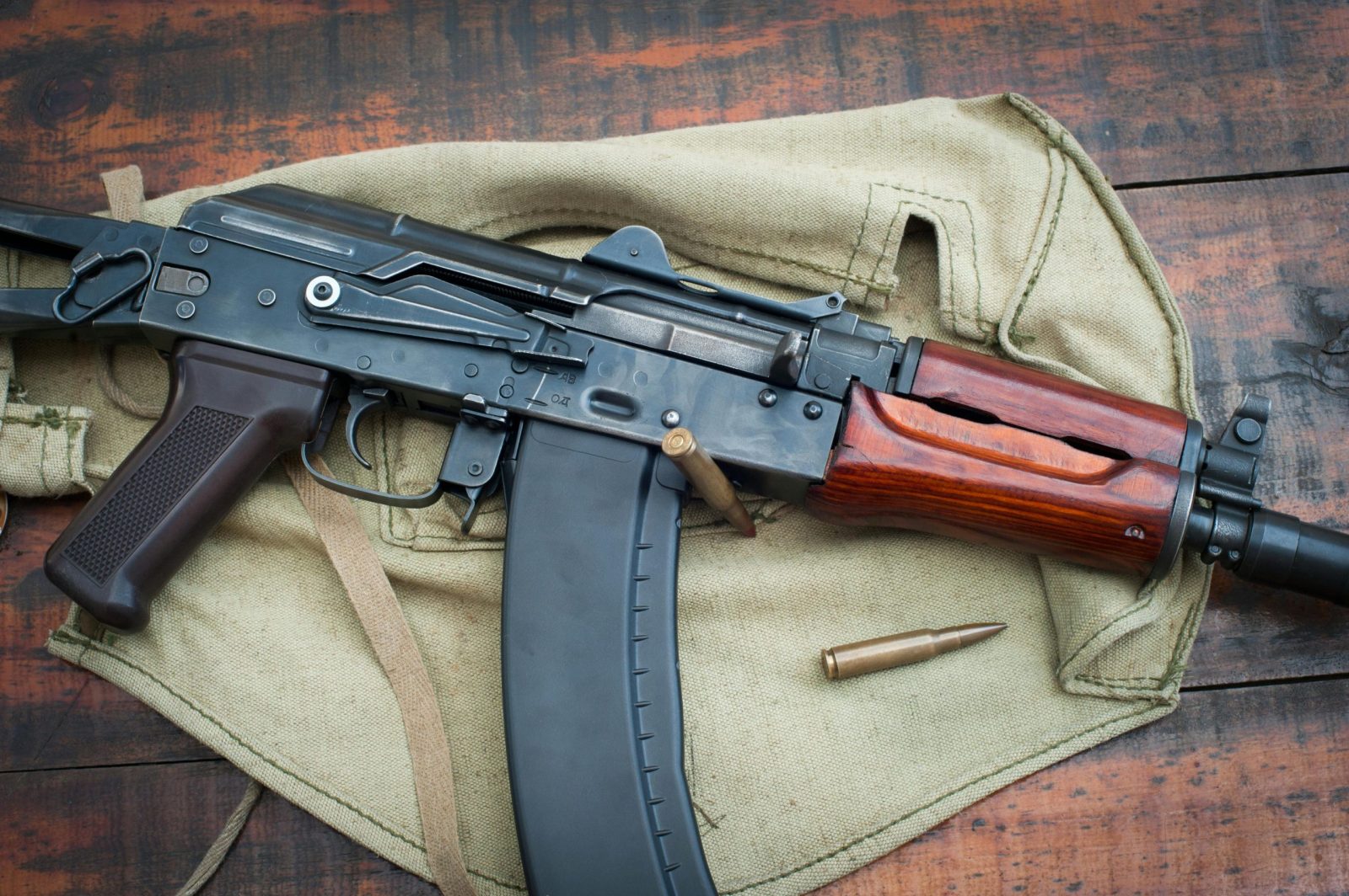 Close-up image of an AK-47 rifle with ammunition on a wooden background.