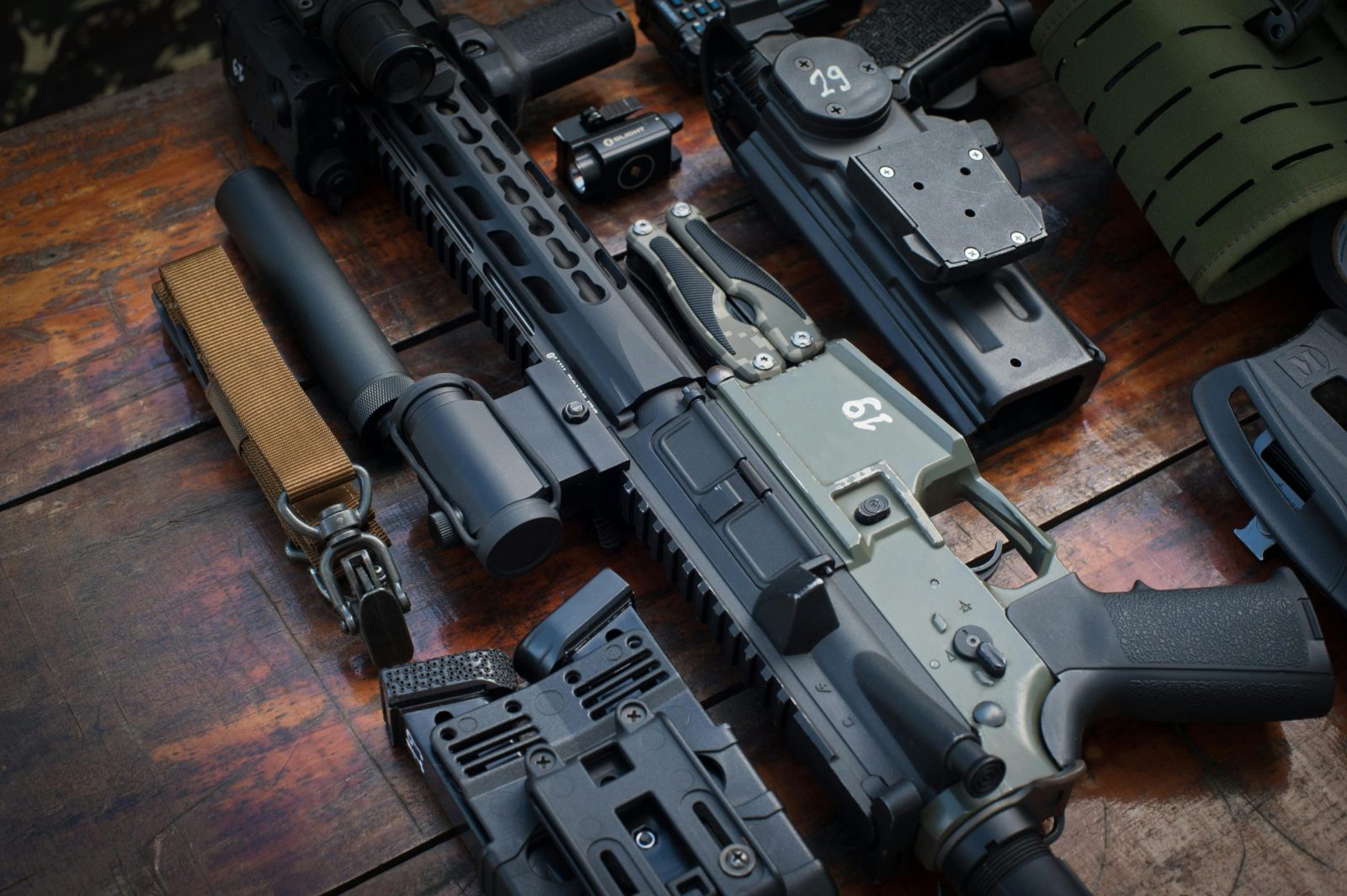 Close-up of tactical firearms and gear arranged on a rustic wooden surface.