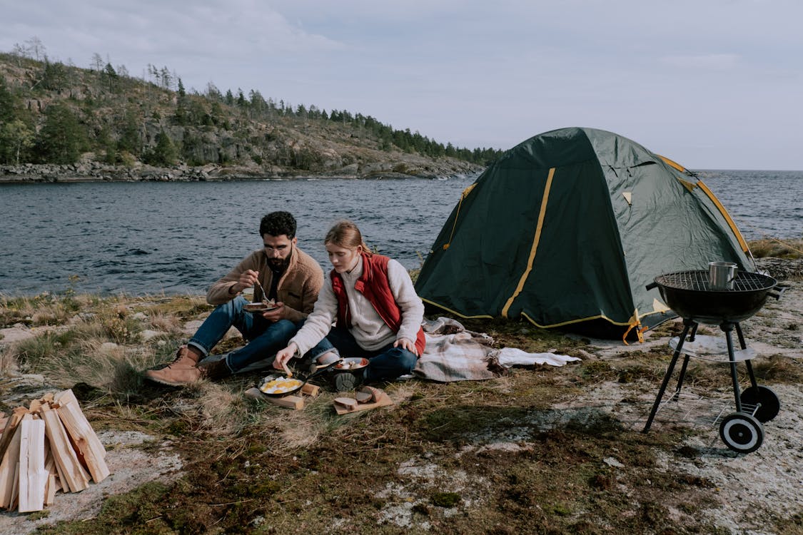 A Couple Sitting on Picnic Mat Near a Tent Along a River