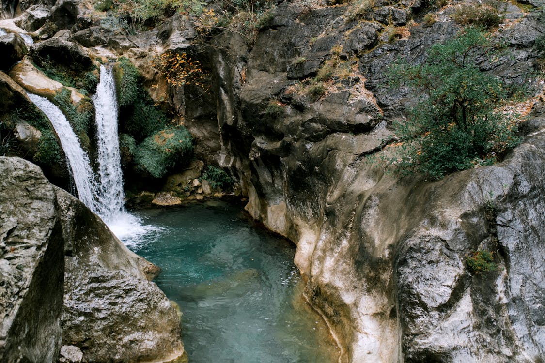 Rocky ravine with waterfall and water stream in mountain terrain