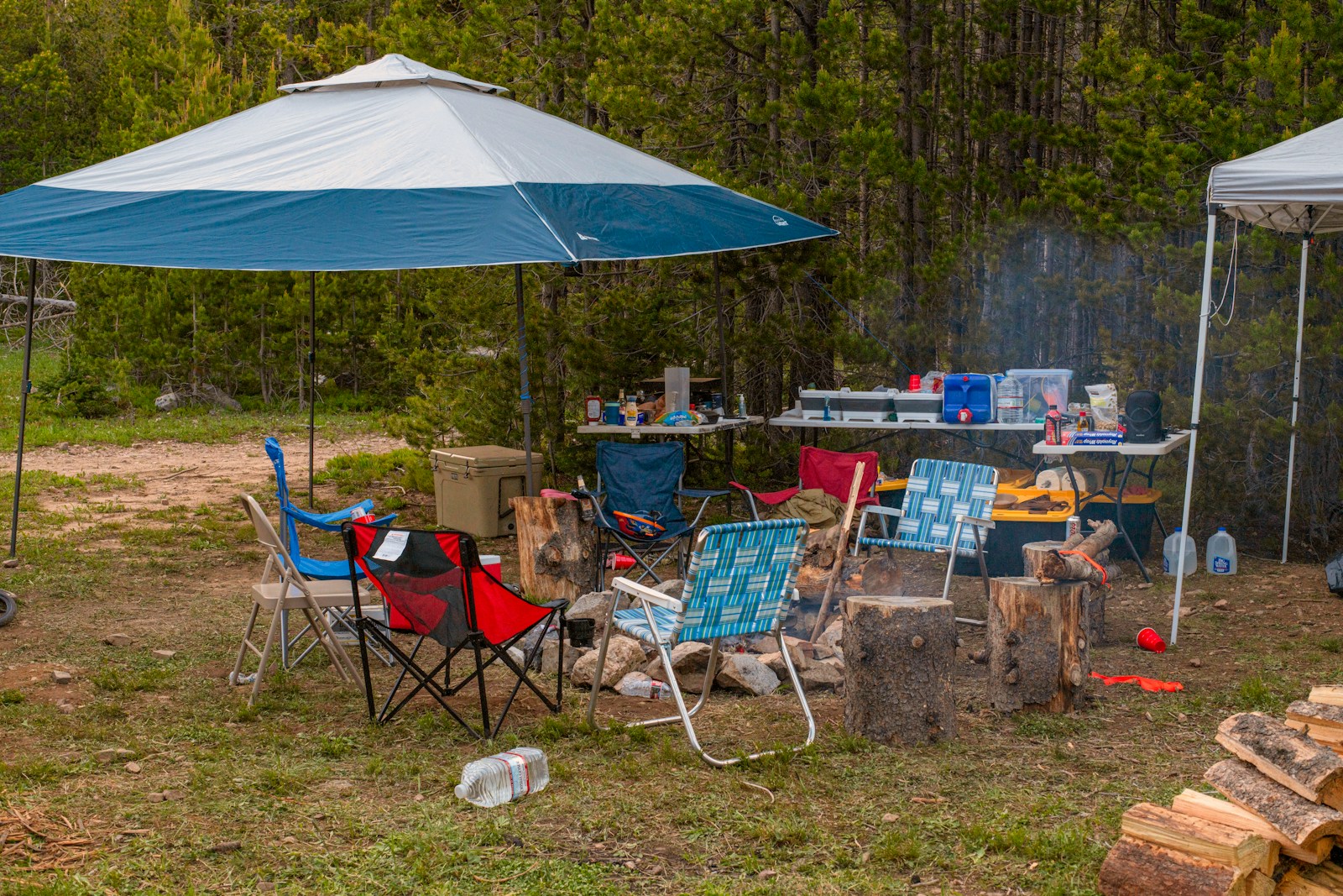 Camping setup: chairs around a campfire with supplies.