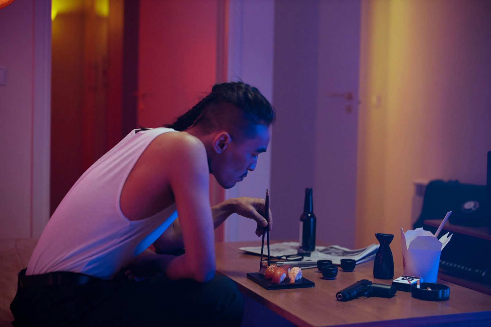 A man eating sushi with chopsticks indoors in a moody atmosphere.