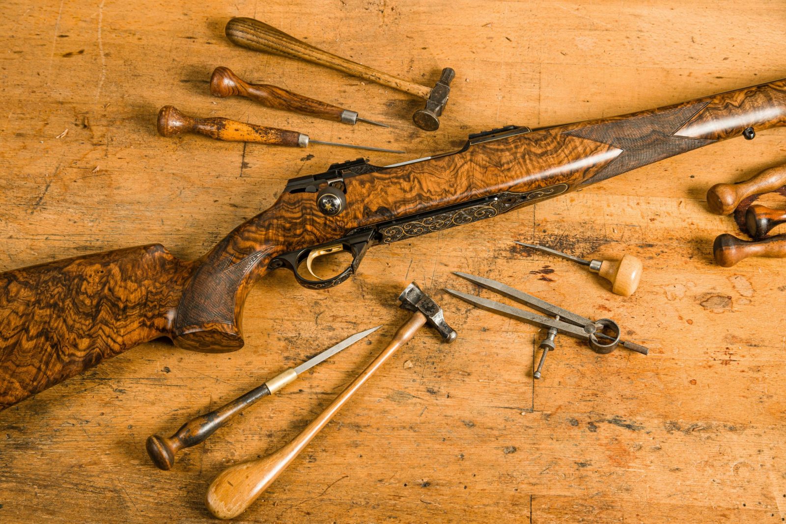 Close-up of a vintage wooden rifle surrounded by antique tools on a rustic workbench.