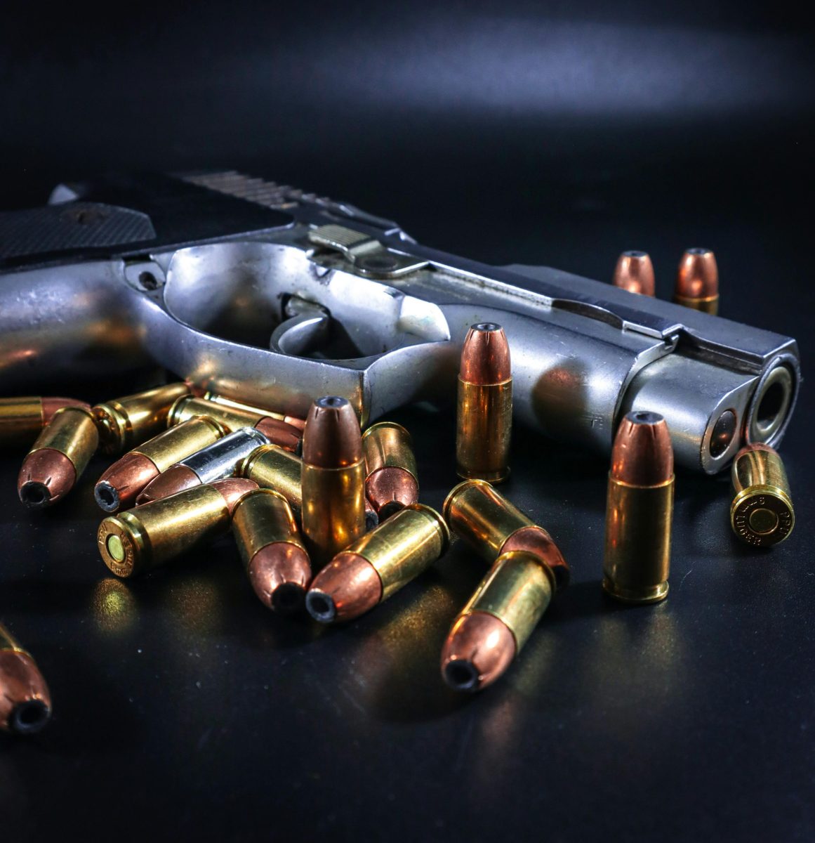 Silver handgun with scattered bullets on dark background, emphasizing danger and weaponry.