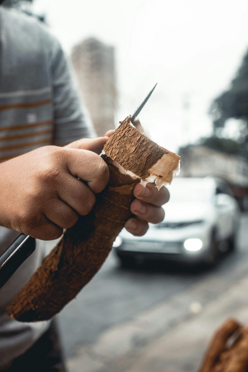 A detailed view of hands expertly peeling cassava with a knife on a busy street.