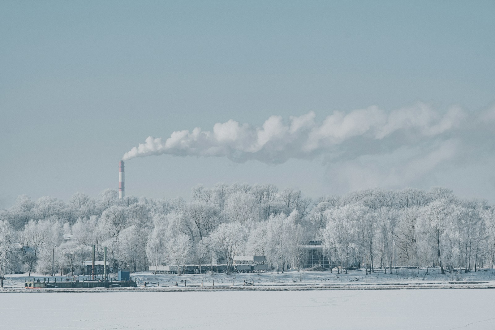 A factory chimney emitting smoke over a snow-covered forest.