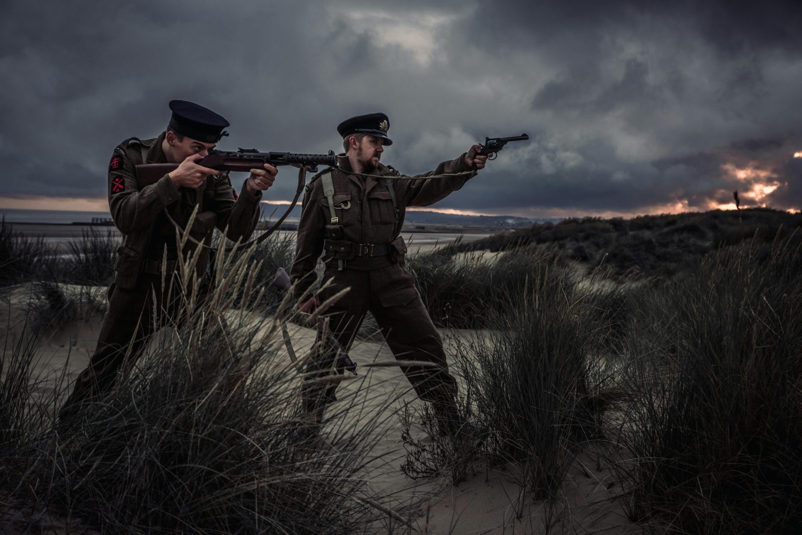 taiki-ishikawa-w6EMxsk8CDA-unsplash Soldiers in uniform train with weapons on a windy beach at dusk, under dramatic skies.