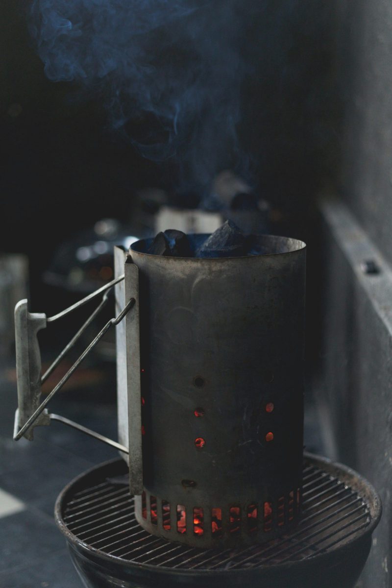 A charcoal chimney starter emitting smoke, set on a grill, prepared for barbecuing.