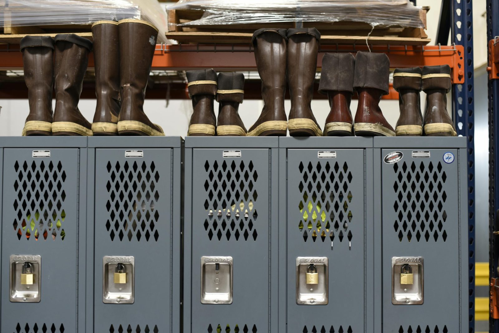 Row of industrial lockers with various rubber boots neatly placed on top in a workspace.