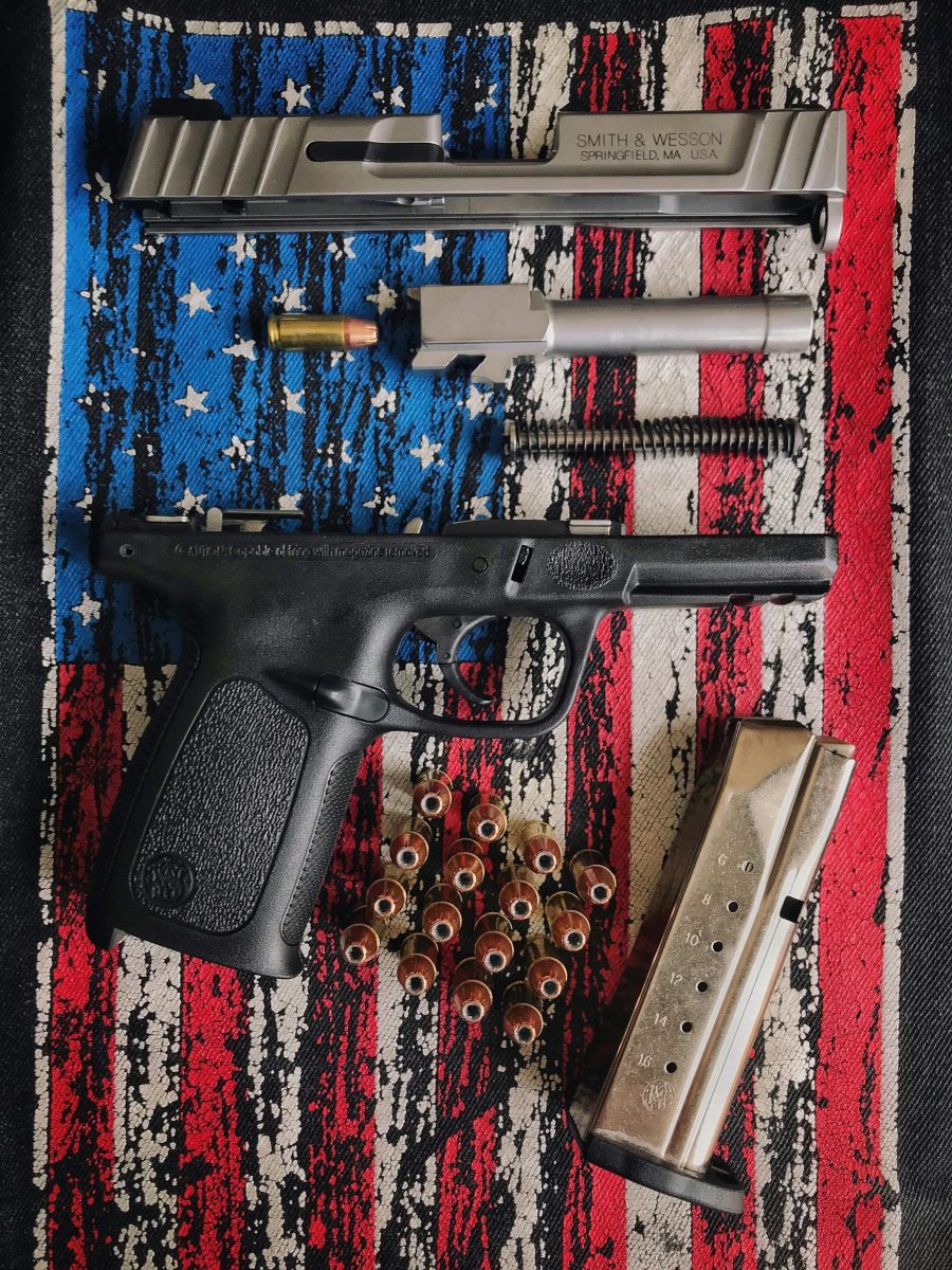 A disassembled firearm displayed on a textured American flag surface, showcasing parts and ammunition.