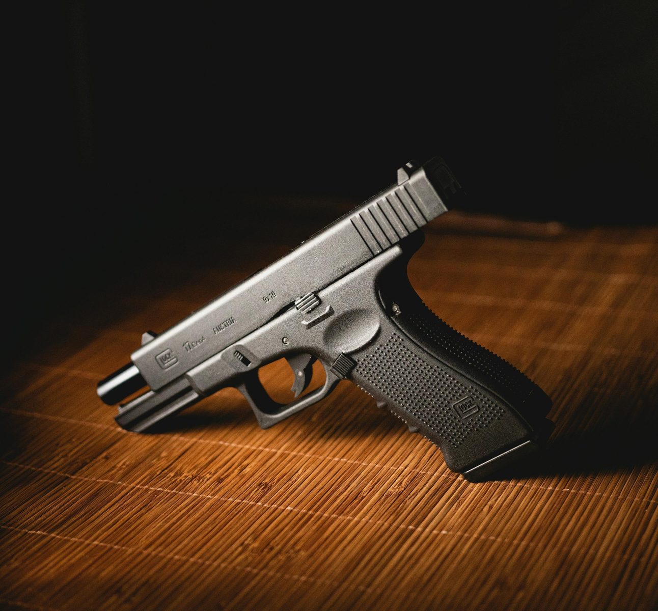 Close-up shot of a modern handgun placed on a bamboo mat, indoors.