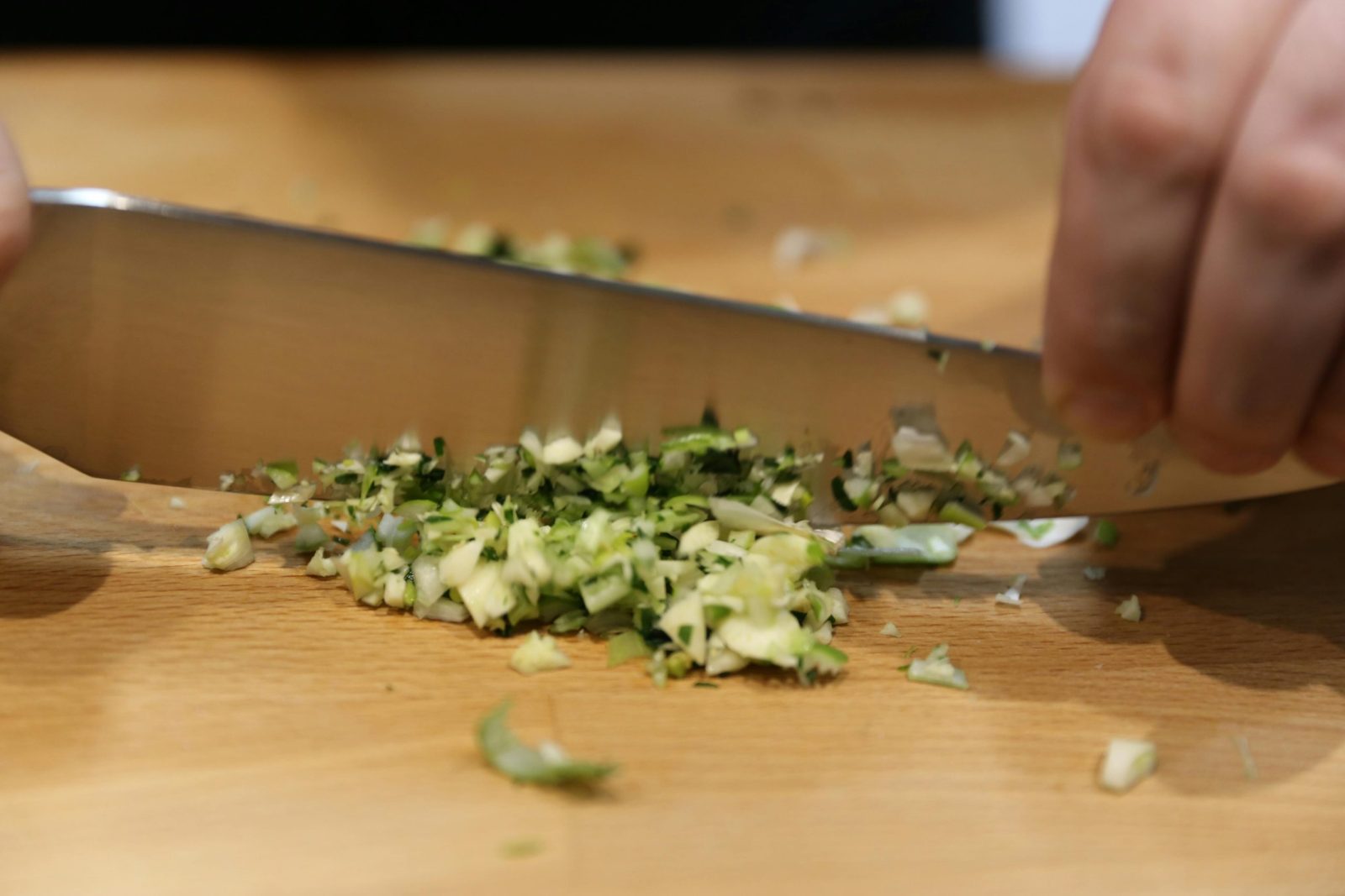A close-up shot of hands chopping fresh herbs with a knife on a wooden cutting board.