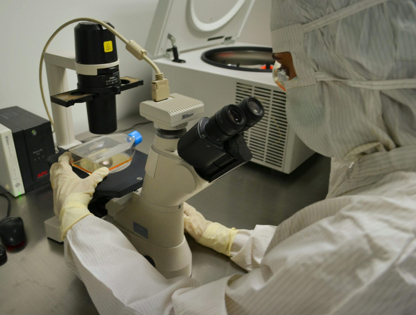Healthcare professional examining specimen under microscope in laboratory setting.