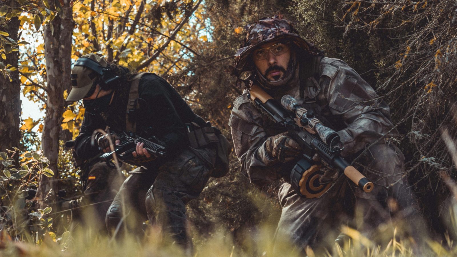 Two soldiers camouflaged in a forest, stealthily navigating with rifles in hand.
