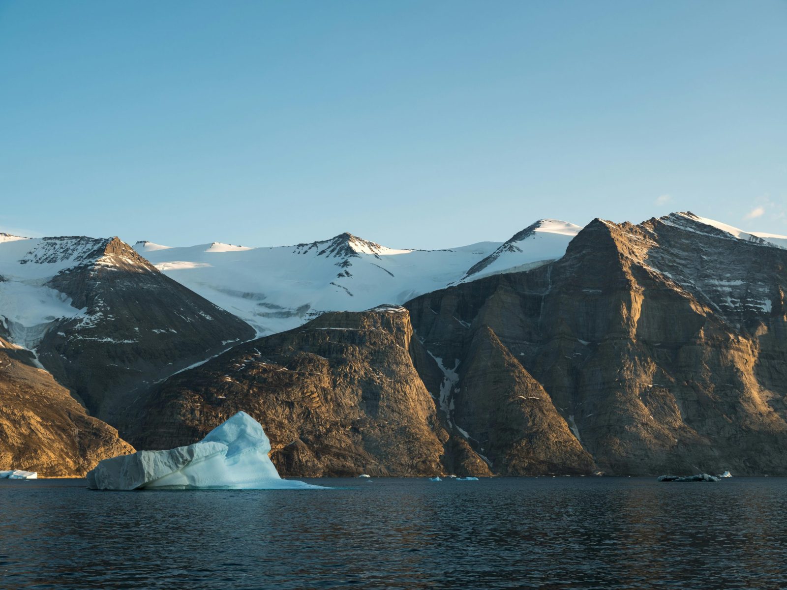 A breathtaking view of icy waters, snow-capped mountains, and icebergs in the Arctic region under a clear sky.