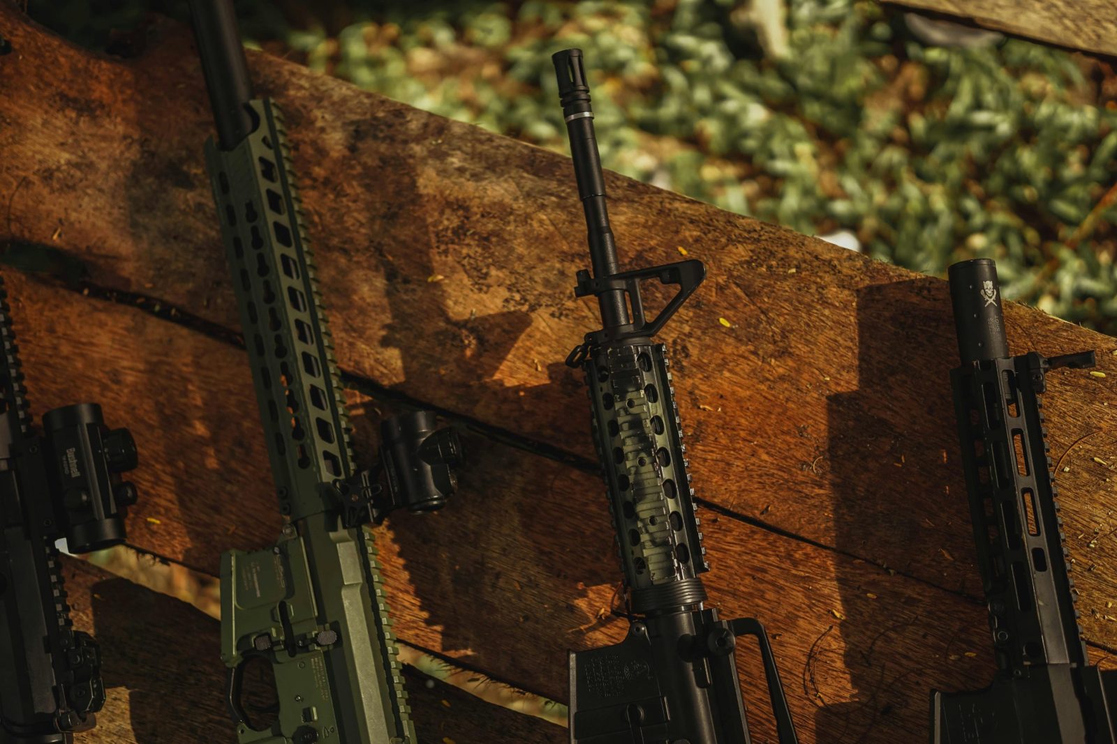 Close-up of rifles laying on a wooden surface outdoors, casting shadows in daylight.