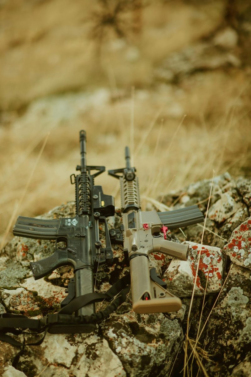 Two military rifles placed on rugged rocks in an outdoor setting.