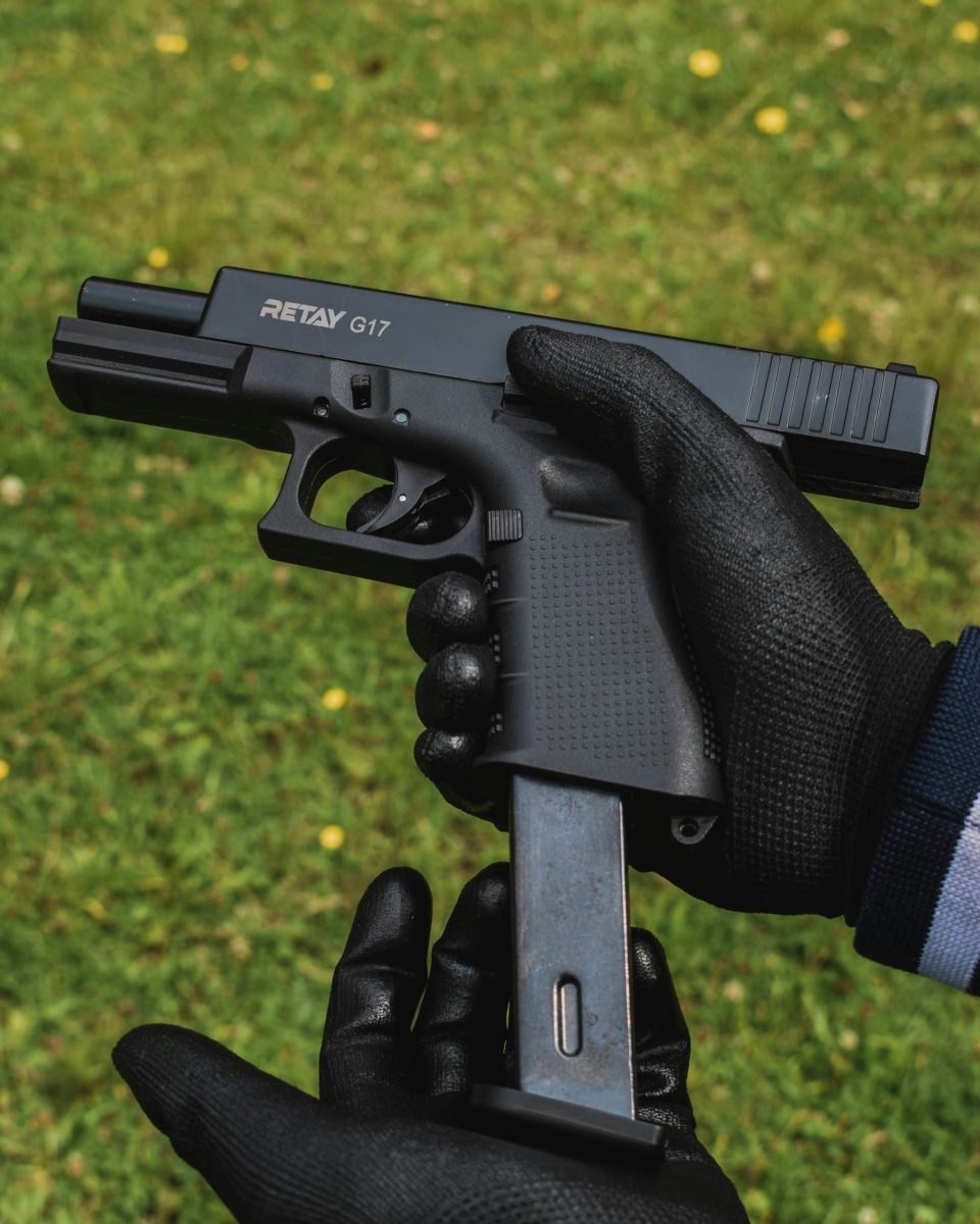 Close-up of hands with gloves holding a disassembled firearm on grass.