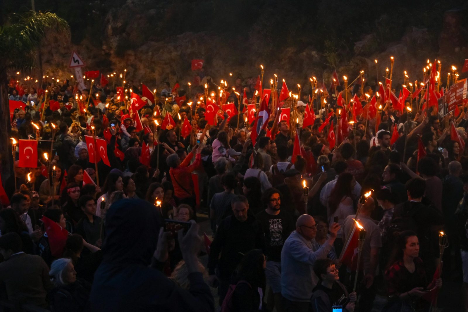 A vibrant crowd gathers for a twilight ceremony with Turkish flags and torches, symbolizing national pride and unity.