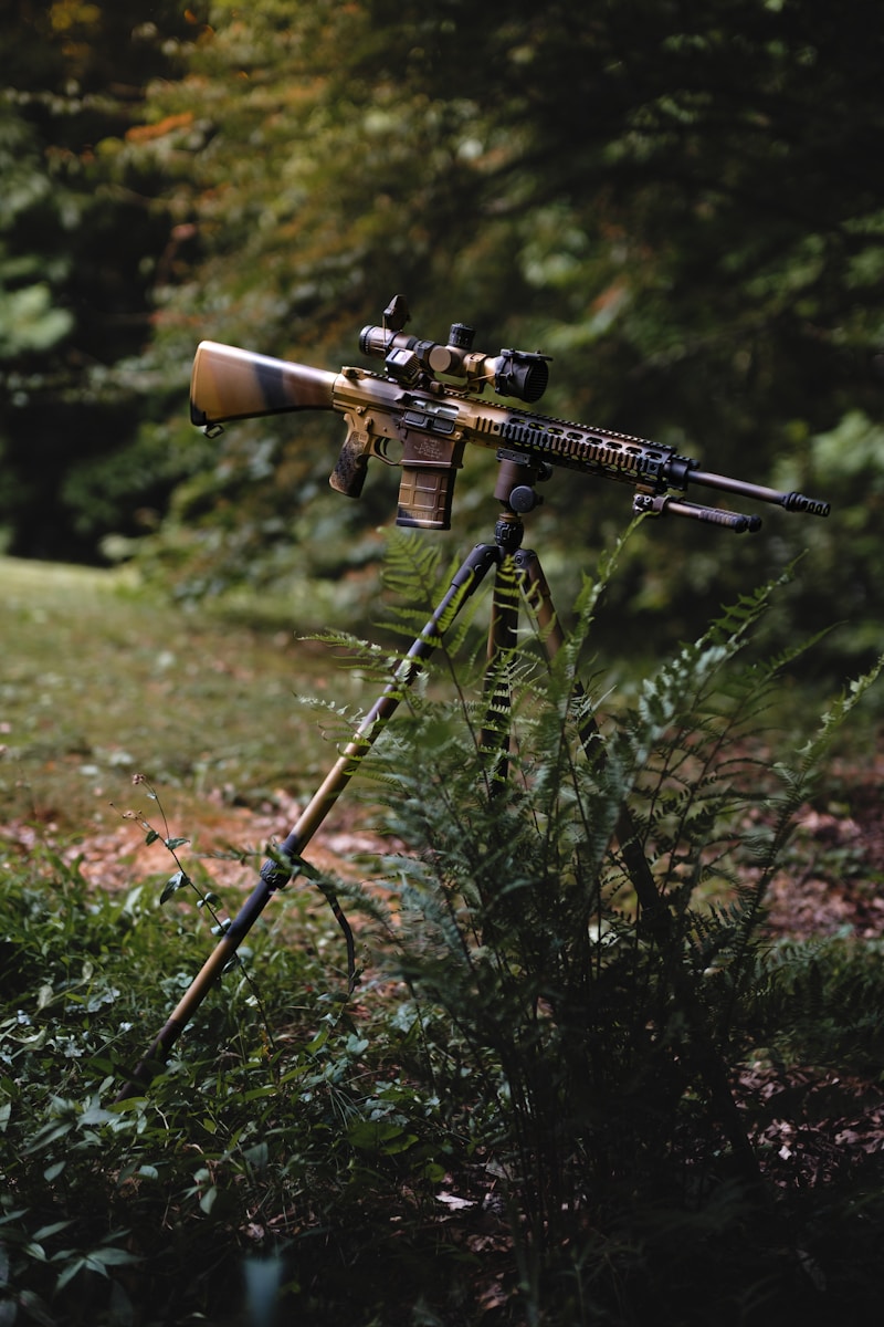 A camouflaged rifle rests on a tripod.