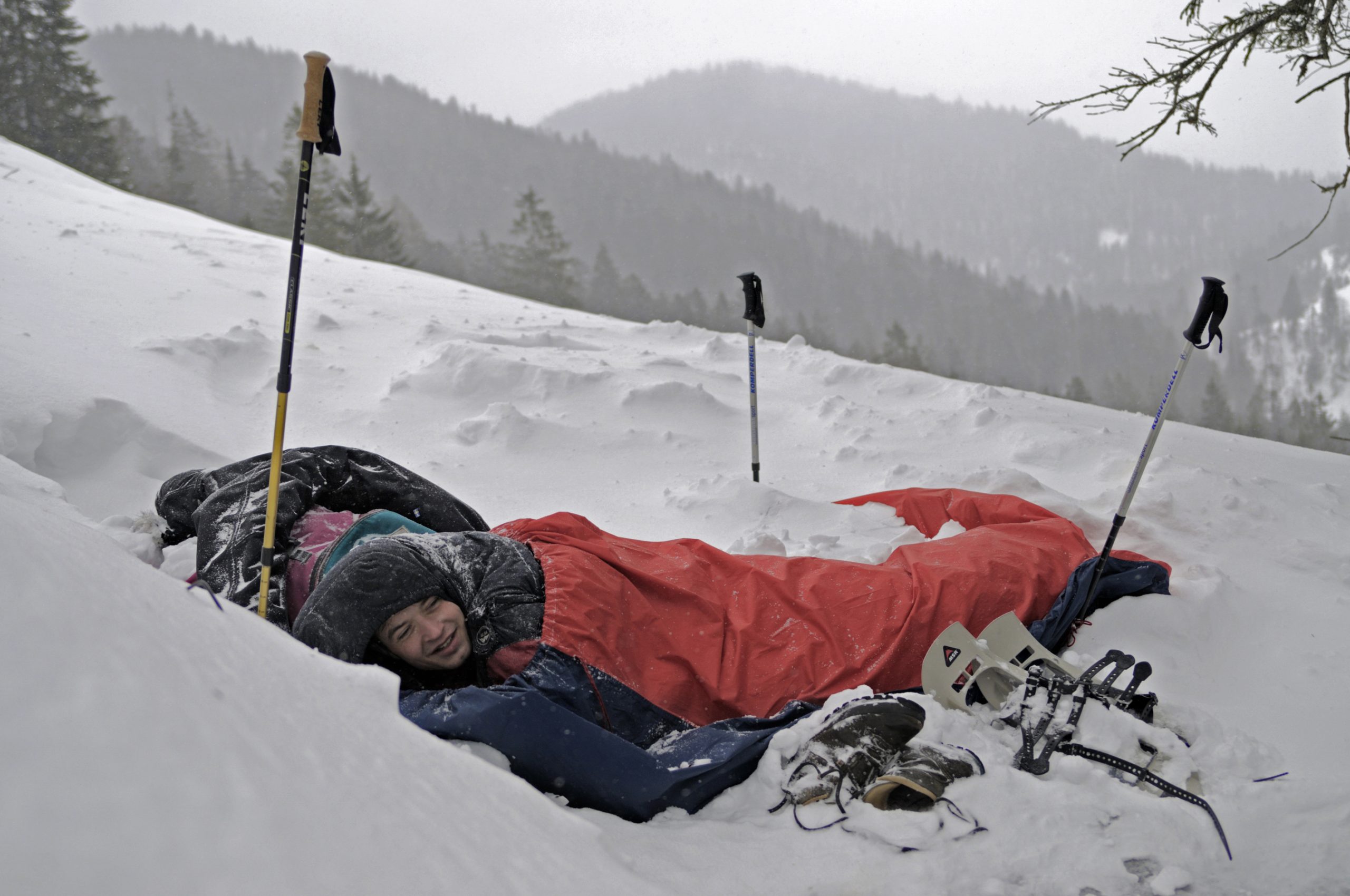 A bivouac sack (in red) covering a man within a sleeping bag in Benediktenwand, Germany