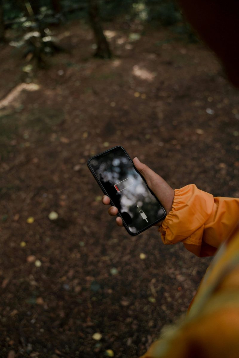 Person in a forest holding a smartphone with a low battery display.