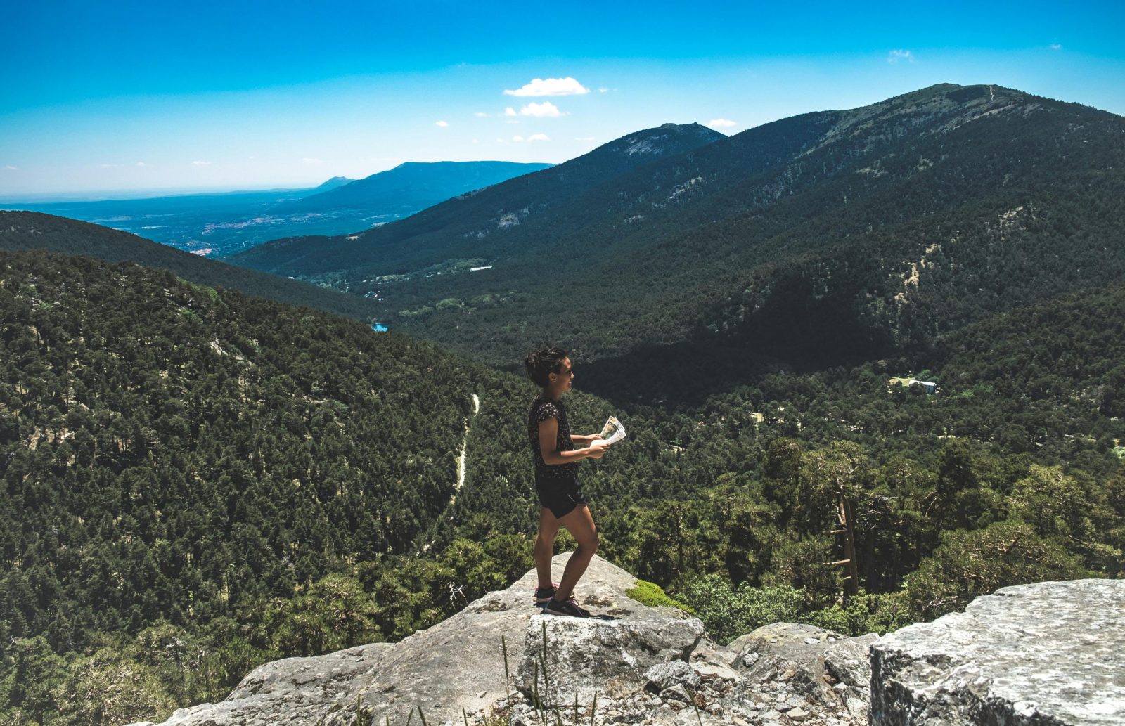 Woman standing on a rock with a map, overlooking a scenic mountain view.