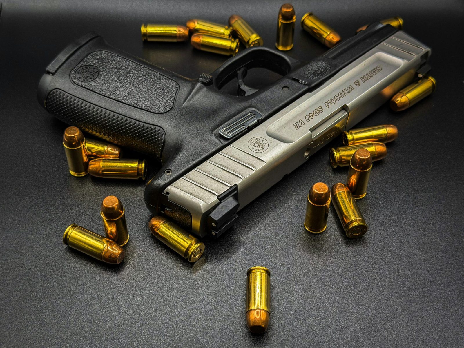 Close-up of a handgun surrounded by bullets, set on a textured black surface for a dramatic effect.
