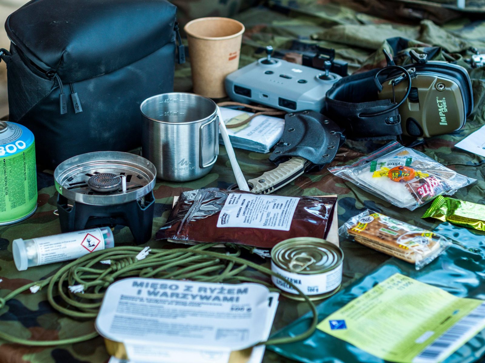 A diverse assortment of camping and survival items laid out, including food, tools, and gadgets.