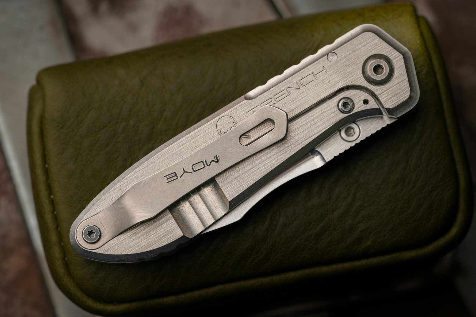 Detailed shot of a folding knife with engraved branding on a textured leather case.