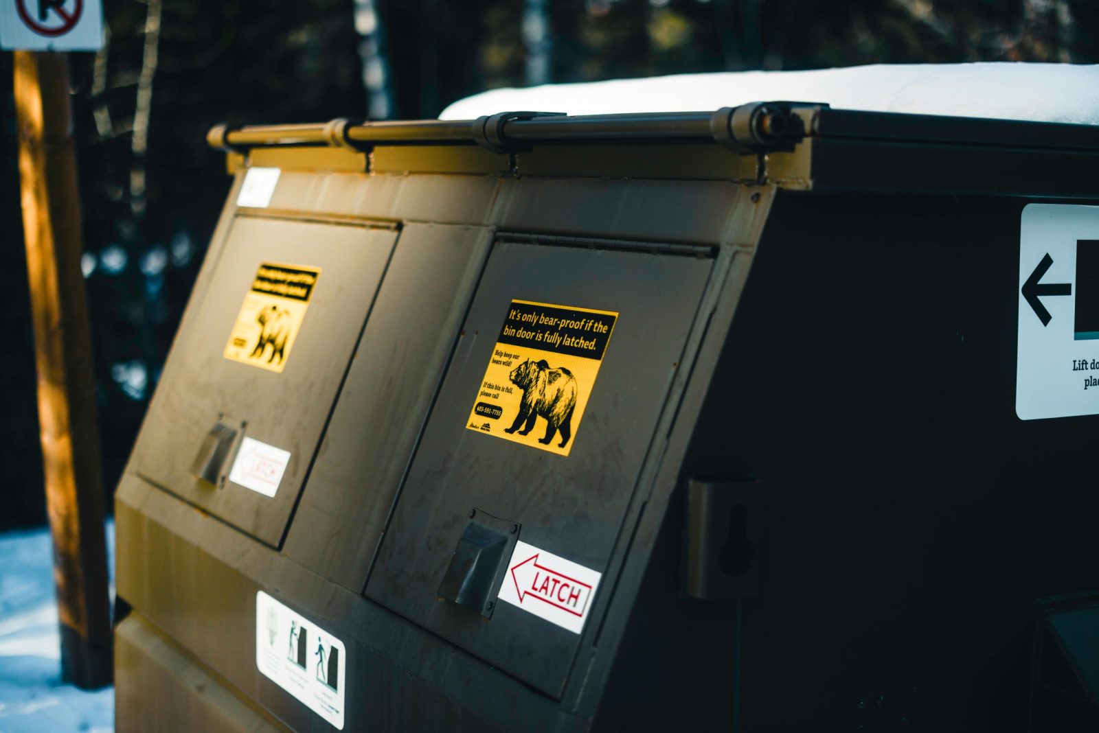 Close-up of bear-proof dumpster with warning signs, emphasizing wildlife safety in Canada.