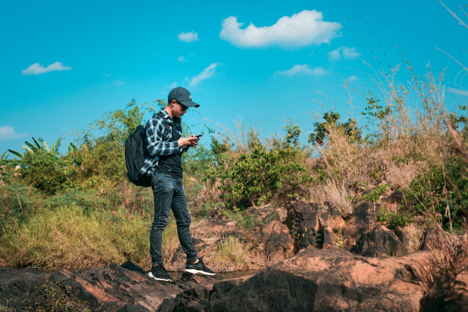 Casual young man exploring nature with smartphone and backpack on a sunny day.