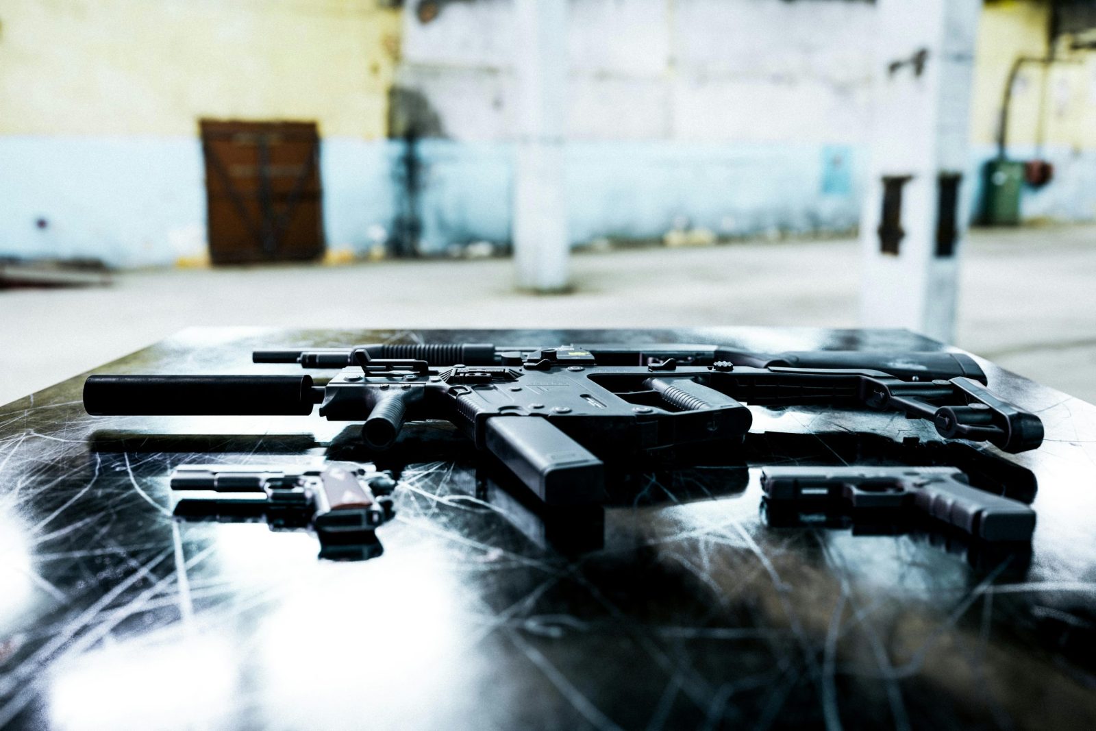 Various firearms displayed on a scratched metal table in an industrial setting.