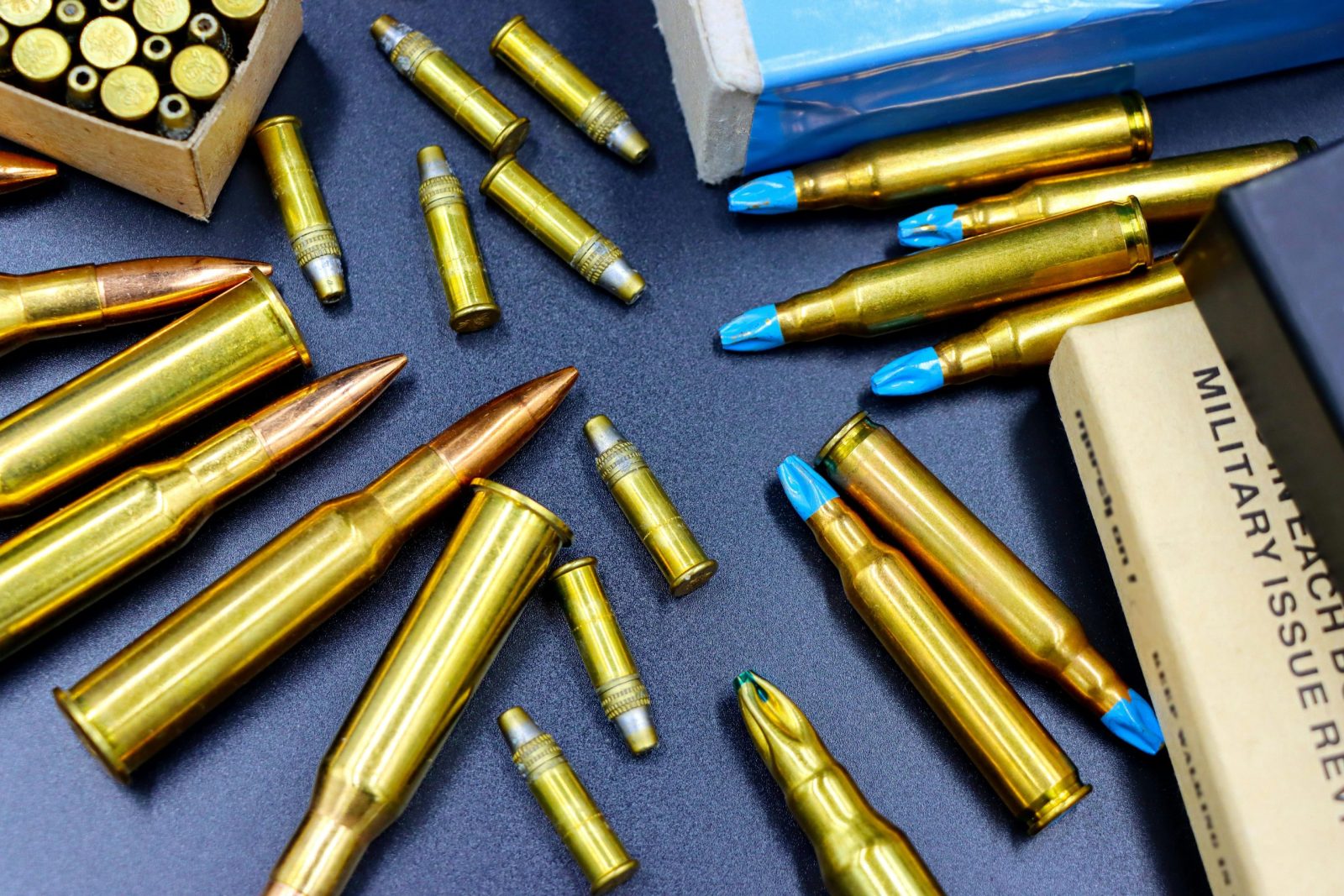 Top view of various rifle and handgun bullets on a dark surface, showcasing their golden casings.